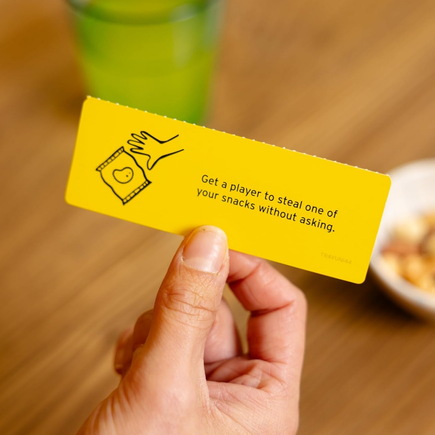 A Hand Holding a Card from Don't Get Got! Travel Edition Over a Wooden Table | Happy