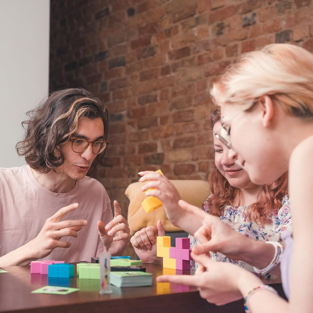 TEAM3 (Green) Board Game (Being Played by 3 People on a Brown Table with a Red Brick Wall Behind) | Happy Piranha
