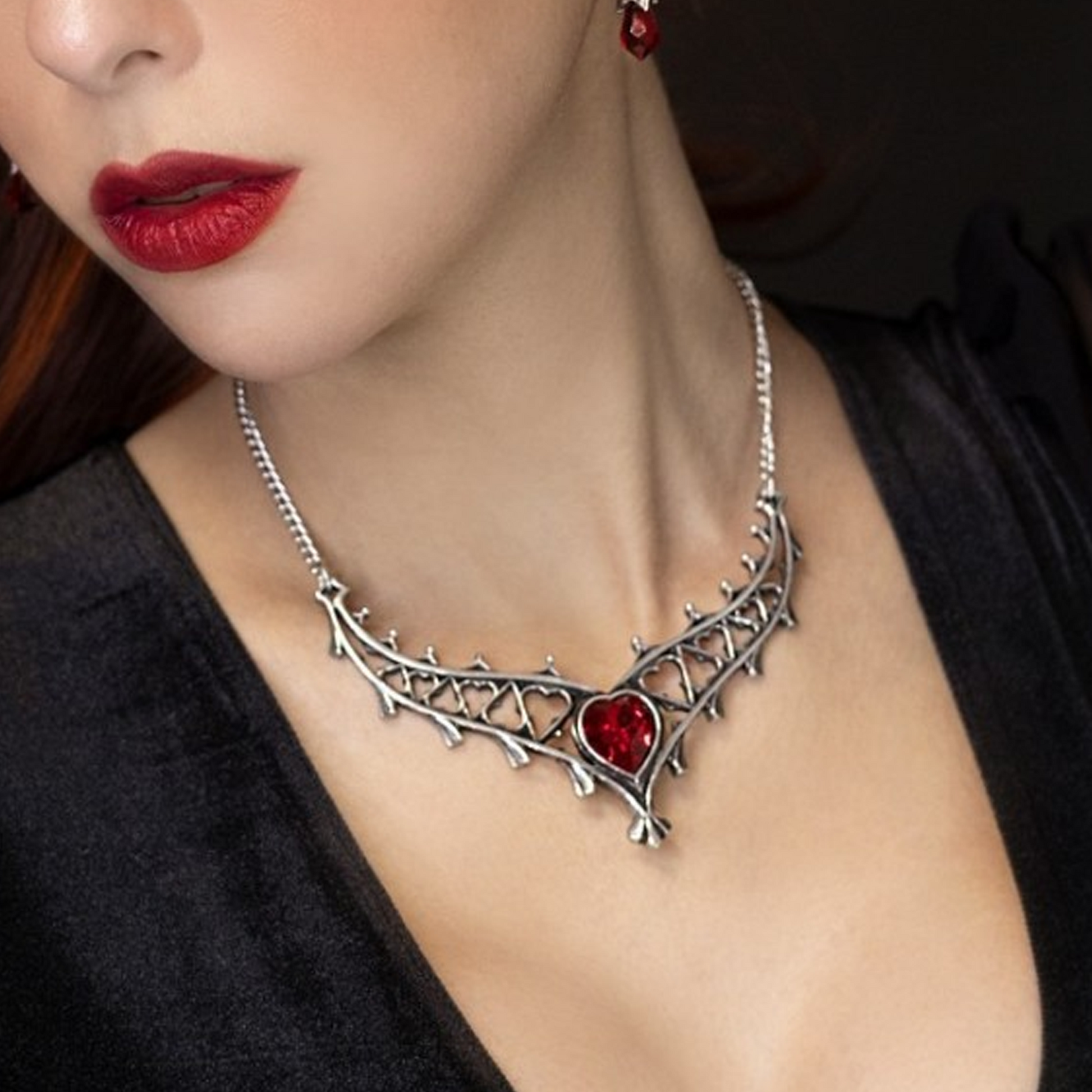 Close-up of a woman with red lipstick wearing an Elizabethan gothic arch design necklace with red heart-shaped stone in the centre on a Dark Background | Happy Piranha