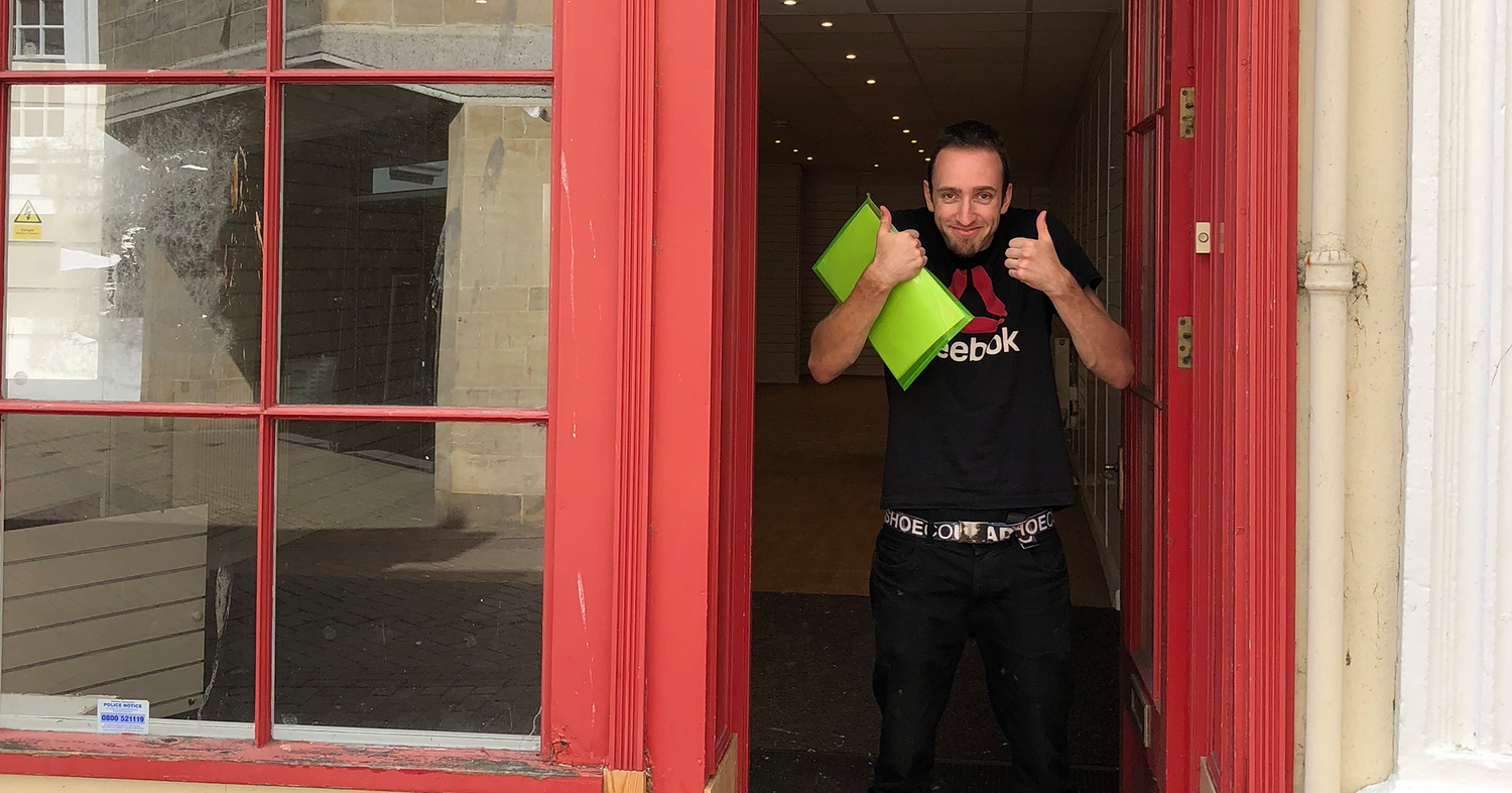 Josh standing in the doorway of the store that is now Happy Piranha, holding the letting documents in his hand and doing a thumbs up gesture.