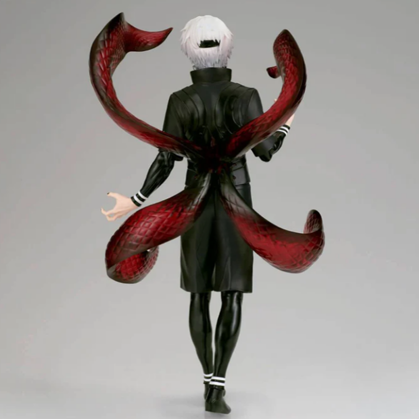 A collectible action figure of the character Ken Kaneki from Tokyo Ghoul, shown from the back with his signature red tentacles spread across his back, wearing a black coat and white hair, set against a plain gray studio background | Tokyo Ghoul Ken Kaneki Grandista Figure | Happy Piranha