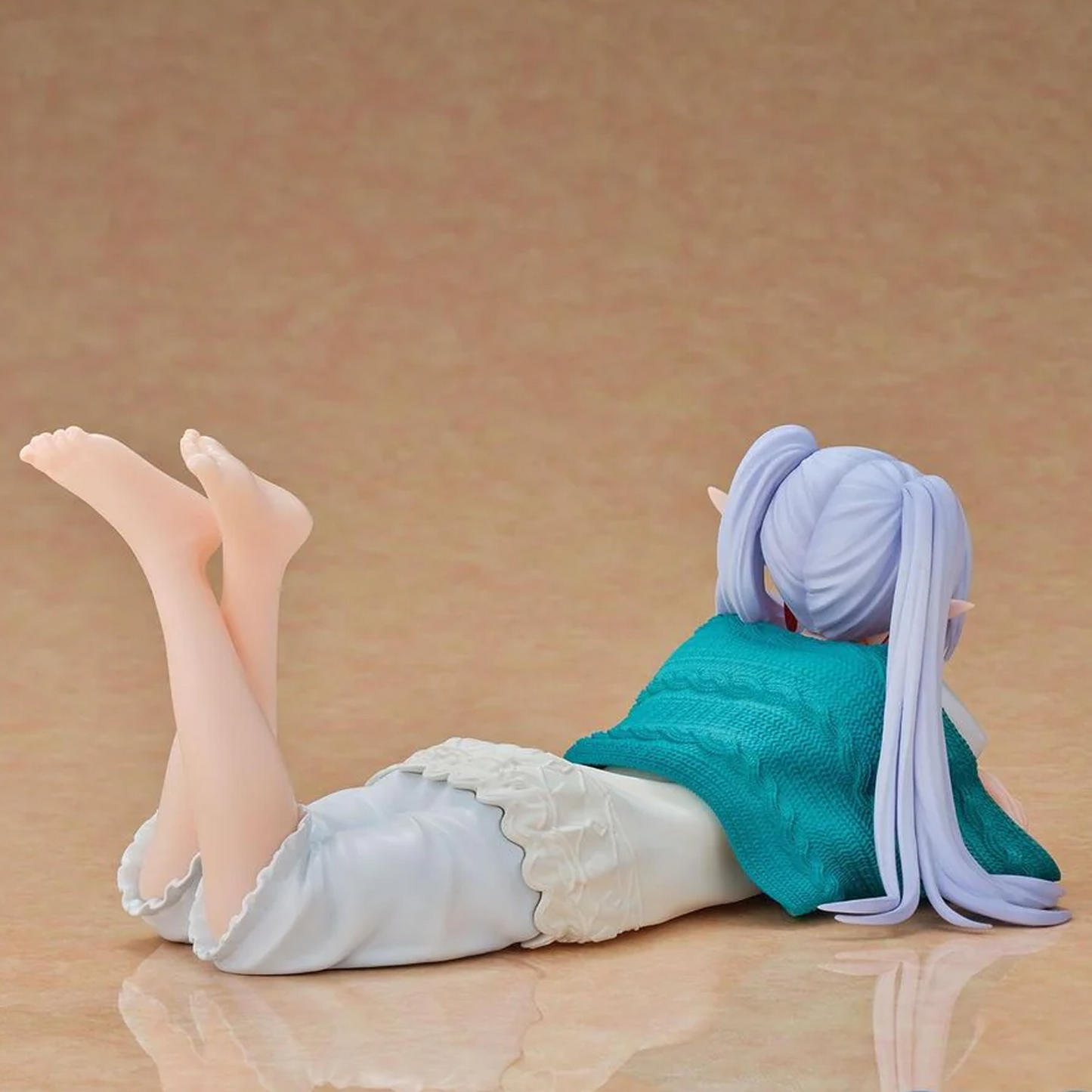 A collectible anime figurine of a character with lavender hair lying on her stomach, wearing a teal top and white skirt, set against a warm beige background | Roomwear: Frieren Beyond Journey's End Yumemirize Figure | Happy Piranha