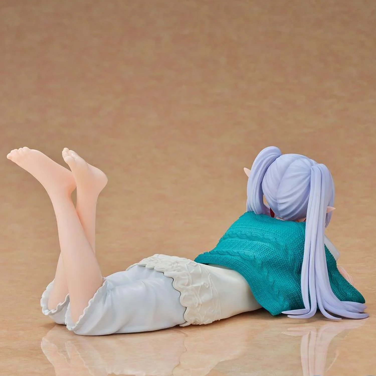 A collectible anime figurine of a character with lavender hair lying on her stomach, wearing a teal top and white skirt, set against a warm beige background | Roomwear: Frieren Beyond Journey's End Yumemirize Figure | Happy Piranha