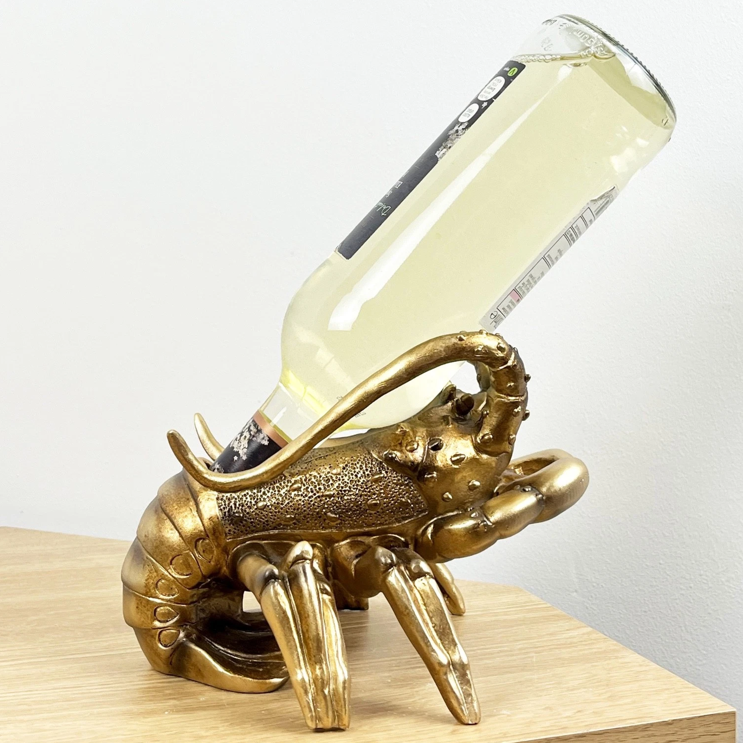 Gold Lobster Wine Bottle Holder Sat on a Wooden Table and Holding a Bottle of White Wine | Happy Piranha