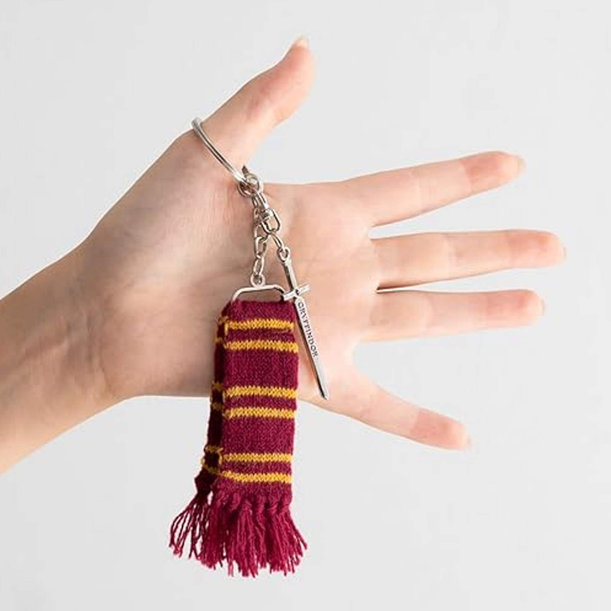 Gryffindor's Sword & Scarf Harry Potter Keychain Hanging of a Person's Thumb on a White Background | Happy Piranha