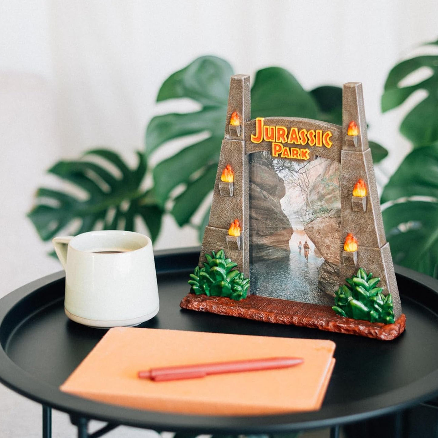 Jurassic Park Gates Shaped 3D Photo Frame on a Black Desk with a White Mug Next to it and a Plant in the Background | Happy Piranha
