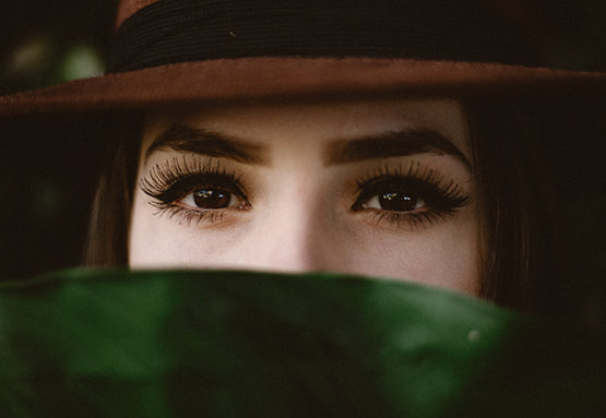 A young lady wearing a brown hat peering over a big green leaf.