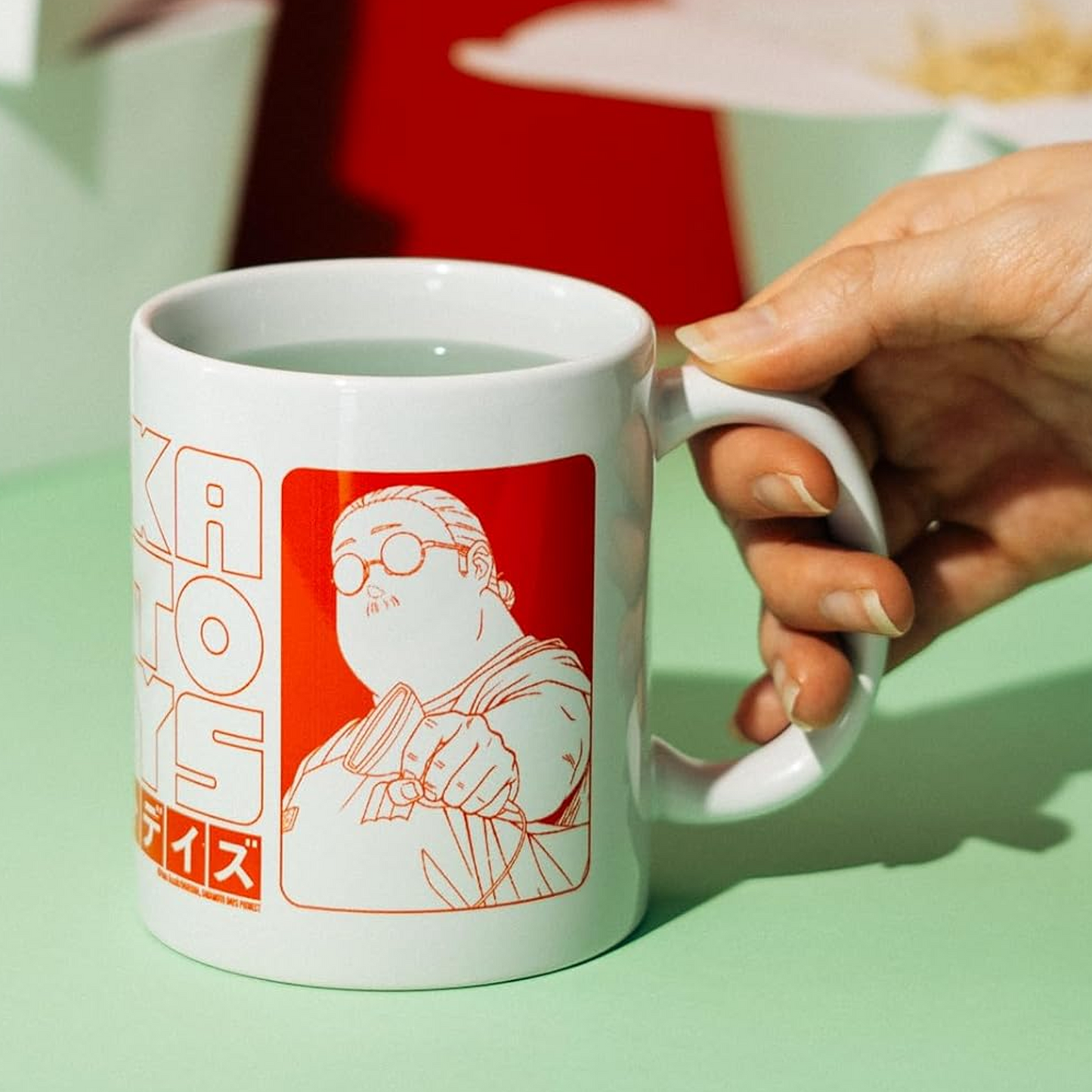 A Red and White Sakamoto Days 350ml Ceramic Mug in a Persons hand on a Light Green Table | Happy Piranha