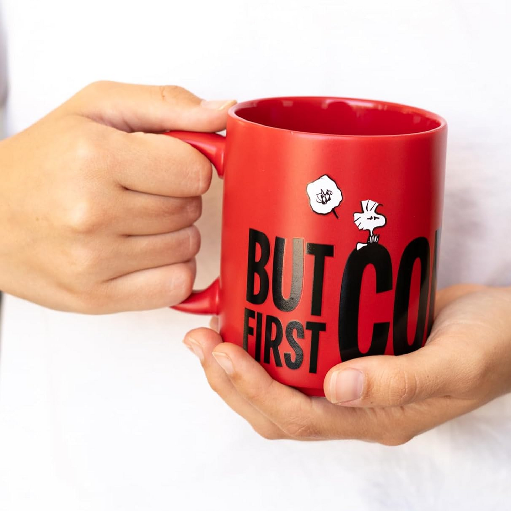 Red mug with 'But First, Coffee' text held by two hands on a white background | Happy Piranha