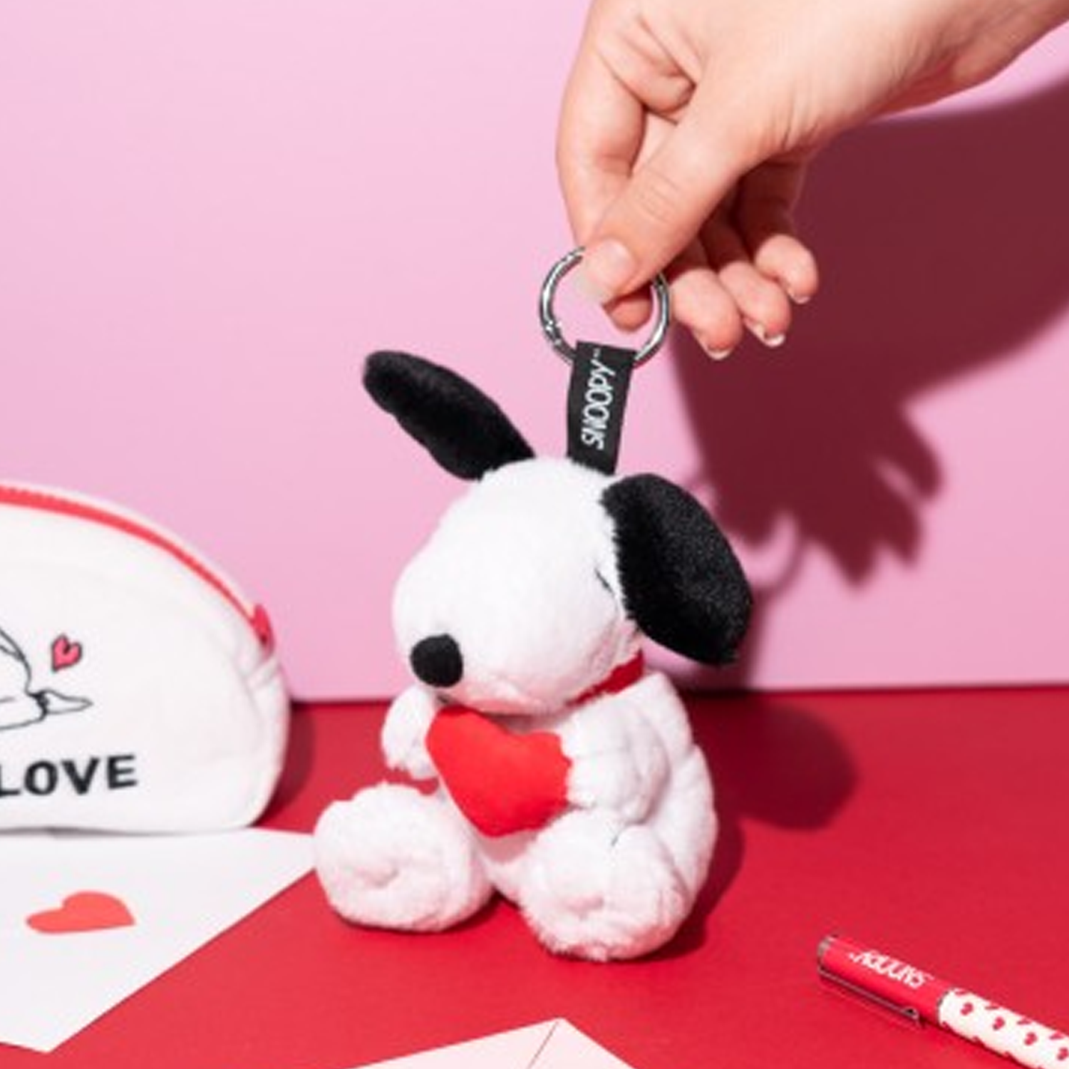 Peanuts: Snoopy Love Season Plush Keychain (Being Held in a Persons Hand on a Pink and Red Background) | Happy Piranha