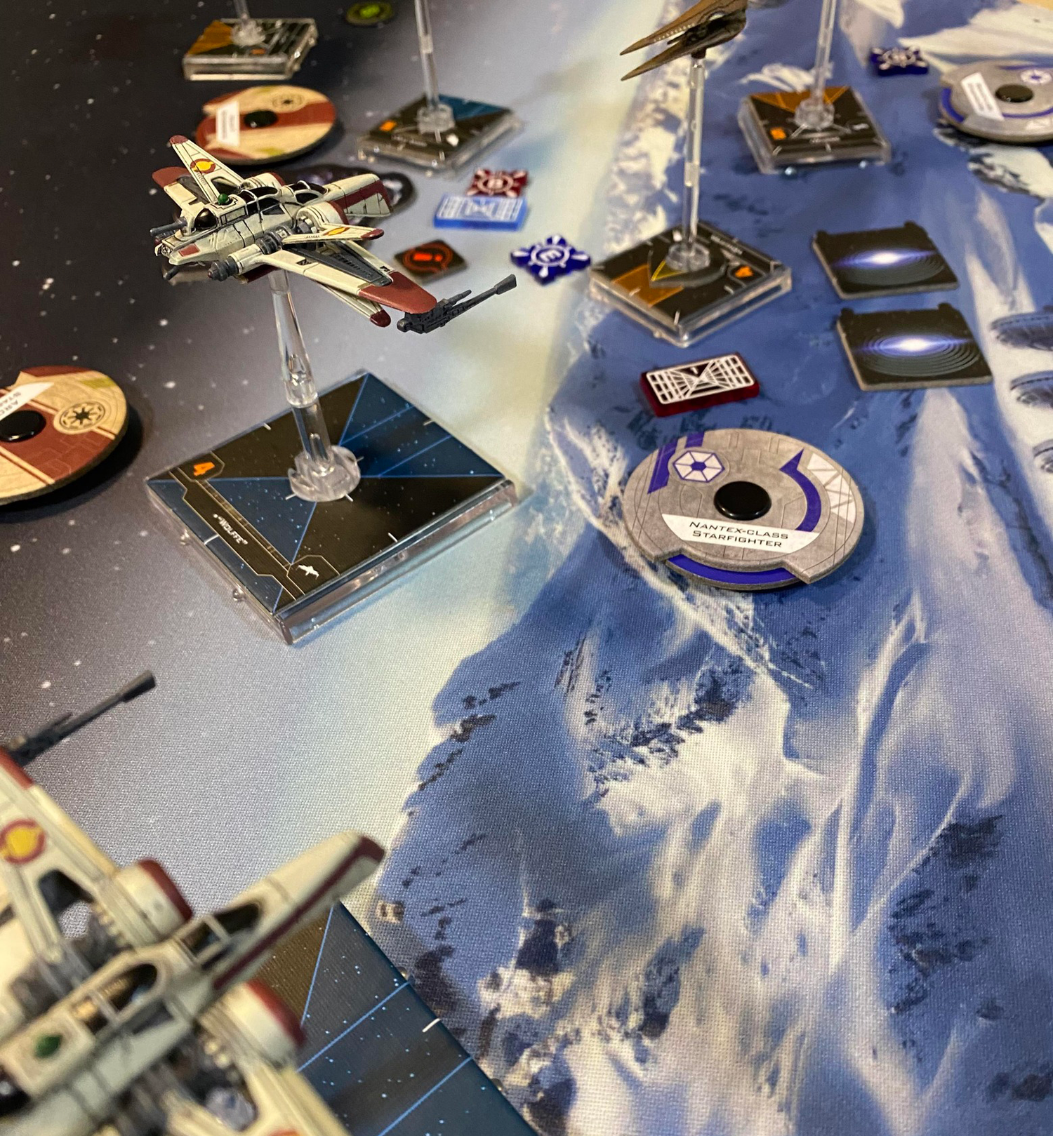 A close up of a game of the Star Wars X-wing Miniatures game  being plated at Happy Piranha café on a winter themed gaming mat.